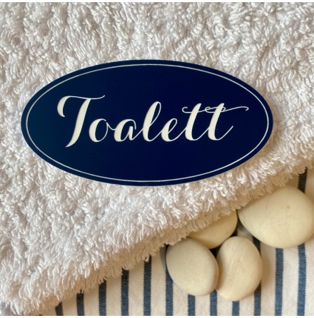 Toalett MAJKEN är en oval skylt med ordet Toalett i vit gravyr på marinblå botten.